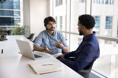 Çeşitli proje yöneticileri çalışma stratejisini tartışıyor, takım çalışması planlıyor, dizüstü bilgisayarla masada buluşuyor, konferans odasında konuşuyor. Hintli işadamı erkek Afrikalı profesyonele görevi açıklıyor