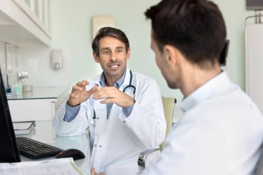 Orta yaşlı Latin doktorların iş yerinde iş arkadaşlarıyla buluşması, profesyonel iş arkadaşlarıyla konuşması, işbirliği, takım çalışması, iş yerinde bilgisayarla oturması, konuşma.