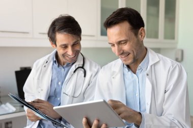 Tıbbi raporlar üzerinde birlikte çalışan iki pozitif erkek doktor, tablet ans belgelerini tutuyor, kayıtları analiz ediyor, sınav sonuçlarını okuyor ve tartışıyor, gülümsüyor, gülüyor, takım çalışmasından keyif alıyor.