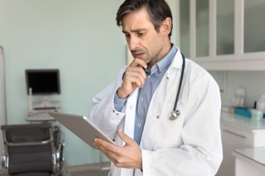 Endişeli yaşlı Latin doktor tabletle ilgili elektronik tıp raporunu okuyor, ciddi teşhisleri analiz ediyor, kötü muayene sonucu, çeneye dokunmak, sağlık hizmetlerinin başarısız olduğunu düşünüyor.