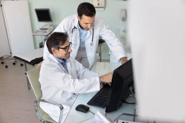 Bilgisayarda tıbbi durumu tartışan iki doktor, bilgisayar monitörünü işaret ederek, elektronik sonuçları birlikte inceleyerek, masaüstünde konuşarak, takım çalışmasından zevk alarak,
