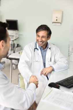 Kendine güvenen sonograf doktor iş yerindeki meslektaşlarıyla el sıkışıyor gülümsüyor, gülüyor, pratik yapıyor ve iyimser bir muayeneden sonra erkek hastayla tokalaşıyor.