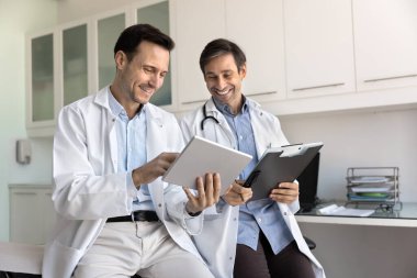 İki tıp arkadaşı elektronik raporu tartışıyor, tabletten kayıtlar okuyor, gülümsüyor, gülüyor. Mutlu Latin doktor danışman iş arkadaşı, cihazı gösteriyor ve işaret ediyor, tavsiye istiyor.