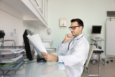 Ciddi profesyonel ultrasonograf doktor ultrason sonuçlarını gözden geçirir, tıbbi kayıtları, geçmişi, muayene raporunu okur, sonografi odasındaki işyerindeki teşhisi düşünür.