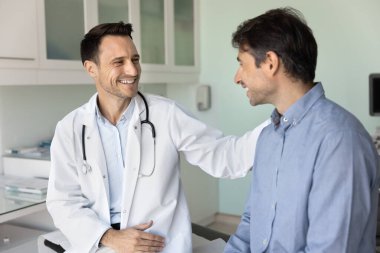 Neşeli destekleyici empatik doktor hasta muayenehanesinde hastanın omzuna dokunuyor başarılı tedavi sonuçları, rehabilitasyon ve iyi bir sağlık kontrolü için tebrik ediyor.