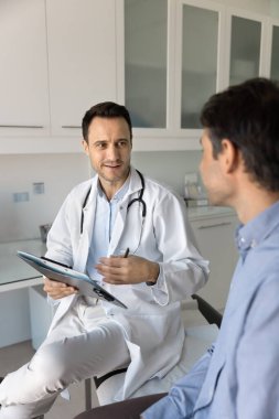 Klinikte randevusu olan, elinde tıbbi kayıtlarla hastayla konuşan, şikayetleri, tavsiyeleri, tedaviyi açıklayan olumlu pratisyen doktor.