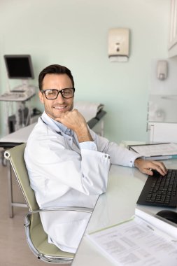 Sonografi odasındaki bilgisayarda çalışan düşünceli bir ultrason uzmanı. Yazıyor, çeneye dokunuyor, başka tarafa bakıyor, gülümsüyor, tıpta başarılı bir kariyer düşünüyor.