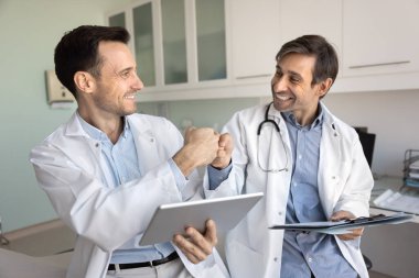 İki pozitif doktor el sıkışır, başarılı takım çalışmasının tadını çıkarırlar, tıbbi raporları birlikte analiz ederler, gülümserler, gülerler, dostluk jestleri yaparlar.