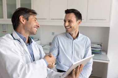 Neşeli Latin bir hasta şükranla doktorla tokalaşıyor, konsültasyon, sağlık kontrolü ve tavsiye için teşekkür ediyor. Latin pratisyen erkek ziyaretçi kliniğiyle el sıkışıyor