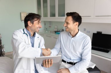 Pozitif başarılı doktor ve mutlu minnettar hasta muayene odasında el sıkışıyor, konuşuyor, gülüyor, gülüyor, iyi testleri tartışıyor sonuç tablet hakkında tıbbi rapor, başarılı tedavi