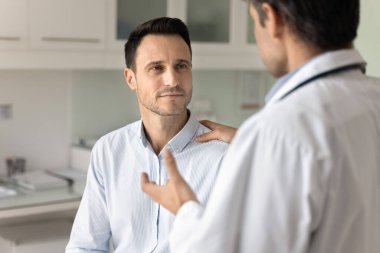Erkek klinikteki hasta hastane ofisini dinliyor, sağlık uzmanını muayene için ziyaret ediyor, teşhis açıklaması, destek, cesaret verici jest, tedavi ve terapi tavsiyesi alıyor.