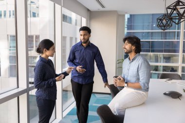 Birçok etnik gruptan genç iş arkadaşları konferans odasında duruyor, konuşuyor, sohbet ediyor, iş stratejisini, iş durumunu, şirket ağlarını, takım çalışması fikirlerini paylaşıyor.