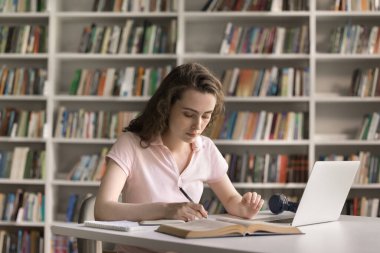 Öğrenci işte. Çalışkan genç kız lise öğrencisi kütüphanede ders çalışıyor. Ders semineri el yazısı denemesi için not defterindeki elektronik uygulamayı kullanarak ödev hazırlıyor.