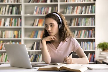 Etkili e-öğrenme. Konsantre olmuş genç kız öğrenci dijital kulaklık takıyor. Sanal sınıftaki öğretmenle iletişim kuruyor. Bilgisayardaki görüntülü sohbet uygulaması.