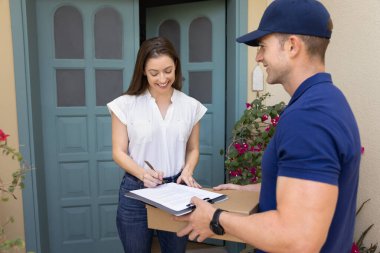 Mutlu alıcı kadın paketini alıyor, alt satırdaki lojistik belgeyi imzalıyor, teslimat kağıdına yazıyor, karton kutu fro alıyor, yakışıklı pozitif kurye, teslimatçı...