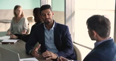 Kendine güvenen genç Hintli iş adamı büyük çalışma masasında erkek iş arkadaşıyla konuşuyor, ortaklık, proje, başlangıç fikirleri, işbirliği şartları, konuşma, dinleme, gülme.