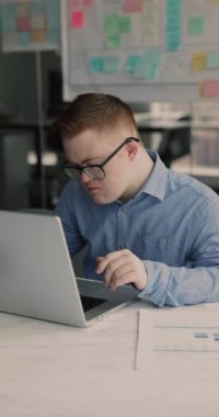 Down sendromlu bir adam ofiste dizüstü bilgisayarda çalışırken gözlük takar, yeni görevleri gözden geçirir, çevrimiçi ödev tamamlamakla meşgul olur, modern teknolojiyi kullanarak yazılım öğrenir. Engellilerin sosyal bütünleşmesi