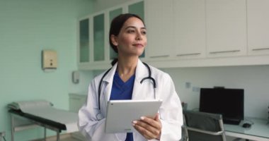 Tıbbi web servisini tablette kullanan olumlu doktor kadın, hastaların geçmişlerini, tıbbi raporlarını, klinik hastalarla online olarak sohbet ediyor, dijital ped tutuyor, yüzünü çeviriyor, düşünüyor.