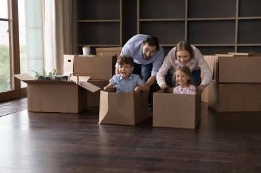 Anaokulundaki küçük oğlan karton kutularda oturan ve taşınma günü mobilyasız oturma odasında neşeli ebeveynlerle eğlenceli oyunlar oynayan yarışlardan hoşlanır. Banka kredisi, yeni ev, mutlu ev sahibi aile kavramı.