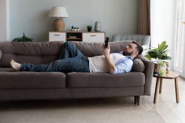 Genç bekar bir adam oturma odasındaki koltukta modern akıllı telefonuyla dinleniyor, haberleri okuyor, internette vakit geçiriyor, mal alıyor, evi arıyor ya da sipariş veriyor. Rahat yaşam konsepti için kablosuz teknoloji