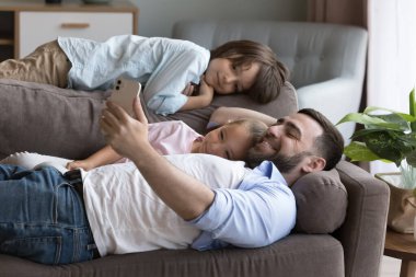Çocuklu baba kanepeye uzanıp eğleniyor, boş zamanlarını akıllı telefon kullanıyor, oyun seçiyor, yeni uygulamaların tadını çıkarıyor, internetten oyuncak alıyor. Genç nesil, modern teknoloji aşırı kullanımı, konfor yaşam konsepti hizmetleri