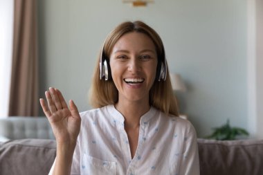 Güzel bir kadın kulaklık takıyor. Arkadaşını selamlıyor. Video konferansına başla. Evdeki kanepeye otur. Modern teknoloji konsepti