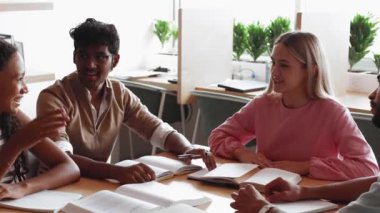 Çok ırklı öğrencilerden oluşan bir grup masada oturup etkin bir takım çalışması yapıyor, kutlama amaçlı beşlik çakıyor, çalışmada başarı jesti yapıyor, mükemmel sonuçlar ve başarı paylaşıyor ve ortak görevi tamamlıyor. Birlik