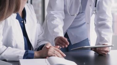 Üniforma giymiş iki kadın doktor, hasta bakımı tartışmalarında, dijital tablet kullanarak tıbbi verileri analiz ediyorlar, kapatıyorlar. İşbirliği toplantısı, profesyonel fikir alışverişi, takım çalışması, teknoloji