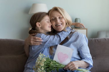 Küçük tatlı kız orta yaşlı büyükannesine sarılıyor. Şefkat dolu bir anın tadını çıkarıyor ve doğum gününü kutluyor. Sevgili torun papatya çiçekleri, yıldönümünde en iyi dilekleriyle gelen kartpostallar.
