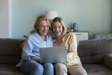 Çekici genç kız ve orta yaşlı anne kahkaha filmi çevrimiçi, dizüstü bilgisayar ekranına bakıyor, e-ticaret sitesi üzerinden elektronik alışverişin tadını çıkarıyor, evde internet üzerinden kaygısız vakit geçiriyor.