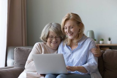Olgun kız ve yaşlı anne kanepede dizüstü bilgisayarlarıyla oturur, malları seçer, internet üzerinden hizmet satın alır, internette birlikte sörf yaparlar. Bilgisayar kullanan, yararlı uygulamalar ve web siteleri gösteren daha genç göreceli öğretim