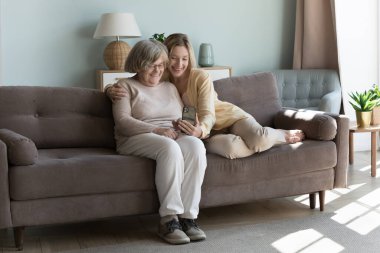 Yetişkin torunu ile ilgilenmek, yaşlı büyükannesini kucaklamak, modern akıllı telefon ekranına bakmak, video görüşmesi yapmak, selfie çekmek, boş zamanlarını telsiz teknolojisi, evdeki internet bağlantısını kullanmak.