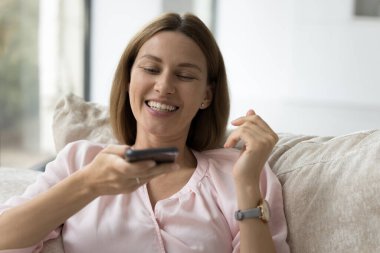 35 'lik çekici kadın akıllı telefonu elinde tutuyor. Hoparlörden arkadaşı ya da ailesini arıyor, yapay zeka bilgileri kullanıyor. Evdeki koltukta oturan modern teknoloji kullanımının keyfini çıkarıyor.