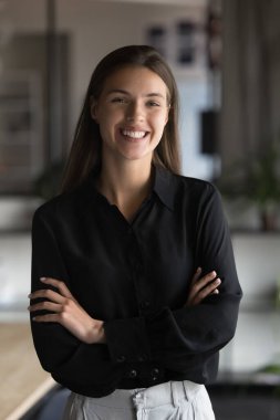 Gündelik siyah gömlekler giyen, gülümseyen, kameraya bakan, modern işyerinde tek başına poz veren, profesyonellik, güven ve kariyerdeki başarıyı gösteren 30 'ların genç ve güzel iş kadınının dikey portresi.