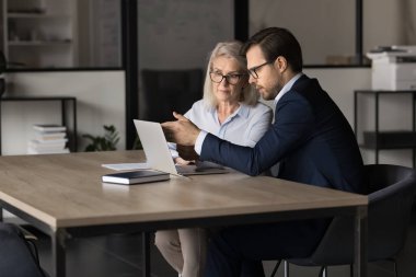 Erkek iş arkadaşları iş yerinde modern dizüstü bilgisayar kullanıyorlar. Müşteriye danışmanlık yapan, bilgisayara işaret eden, hizmetlerin açıklamalarını sunan, çevrimiçi e-bankacılık uygulamasını veya e-hizmetleri açıklayan banka yöneticisi