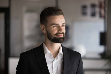 Resmi ceketli dalgın bir iş adamı uzaktan gülümseyerek bakıyor, kariyer gelişimi ve tanıtımından memnun, profesyonel başarılardan, gelişmelerden, kafadan vuruşlardan mutlu görünüyor.