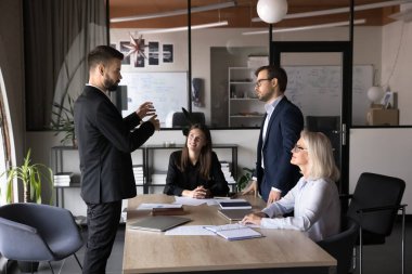 Kendine güvenen iş adamı, modern konferans odasında beyin fırtınası toplantısı hakkında iş arkadaşlarıyla konuşuyor, ortak proje için fikirler sunuyor, iş stratejilerini tartışıyor, tartışıyorlar. Yönetim, takım çalışması