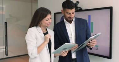 Tablet üzerindeki kağıt ve çevrimiçi içerikleri karşılaştıran, sunum tahtasında duran, pazarlama verileri üzerinde çalışan, konuşan, gülümseyen mutlu çeşitli iş arkadaşları.