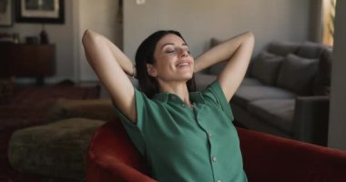 30 'lu yaşlarda rahat bir şekilde giyinen güzel bir kadın rahat koltukta oturup, ellerini başının arkasına koyuyor, gözleri kapalı hayal kuruyor, gevşiyor ve sorunsuz bir hafta sonu evde tek başına vakit geçiriyor.