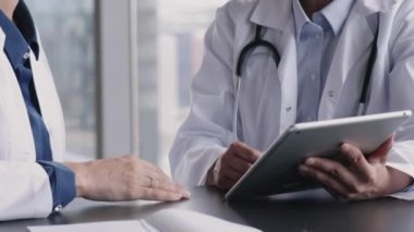 Tablet kullanan iki doktor, hasta davasıyla ilgili profesyonel tartışmalara öncülük ediyor, klinikte tıbbi uzlaşma sırasında görüşlerini paylaşıyor, el sıkışıyor, görüşmeyi bitiriyor, karşılıklı saygıyı dile getiriyor, kapatıyor.