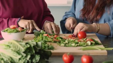 Anne ve yetişkin kızın birlikte yemek pişirdiği, bıçaklar tuttuğu ve doğal beslenme yemeği için tahta tahtada taze sebzeleri doğradığı kesikli manzarayı kapatın. Aile yemekleri, sağlıklı yiyecekler ve tarifler.