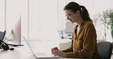 Genç 30 'lu yaşlarda çekici bir kadın, çağdaş ofiste dizüstü bilgisayarda çalışırken gözlük takıyor, e-postalara cevap veriyor, verileri analiz ediyor, belge hazırlıyor ya da araştırma yapıyor. İş, teknoloji