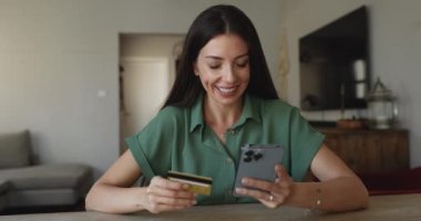 Genç bir kadın akıllı telefon ve kartla masada oturuyor, elektronik ödemeyle ilgili sorunlar yaşıyor, kaynak yetersizliği, dolandırıcılık veya dolandırıcılık yüzünden başarısız internet işlemlerini reddediyor,