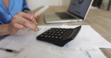 Kapat kadın hesap makinesi, dizüstü bilgisayar, inceleme faturaları, kağıtlar, finansal yönetim ve bütçe işleriyle meşgul olarak masada oturuyor. Kişisel ya da iş harcamalarının izlenmesi, giderlerin hesaplanması, gelirlerin izlenmesi