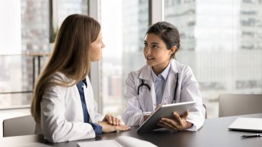 Klinikte ortak görev üzerinde çalışan iki ciddi kadın doktor, modern dijital tabletle masaya oturmuş, görüşlerini, düşüncelerini ve çözümlerini paylaşıyor, tedavi planını gözden geçiriyor, düzeltmeler yapıyor.