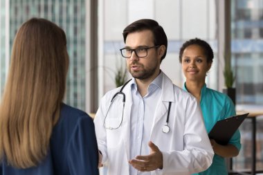 Dikiz manzaralı hasta ayakta duruyor, özel kliniğe yaptığı ziyarette erkek doktoru dinliyor, profesyonel sağlık hizmetleri tavsiyeleri alıyor, hastanedeki randevusunu tamamlıyor. İlaç, sigorta, bakım