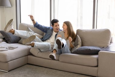 Neşeli genç İspanyol çift evdeki yeni rahat kanepeye düşüyor, rahat bir dairede eğleniyorlar, birlikte eğleniyorlar, gülümsüyorlar, bağırıyorlar, eğleniyorlar, eğleniyorlar.