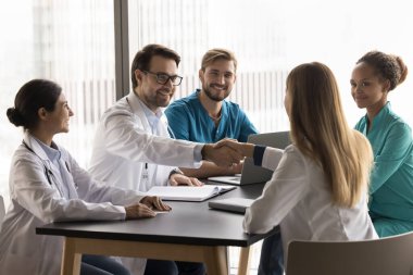 Bir grup sağlık çalışanı masanın etrafında toplandı, takım toplantısını başarıyla tamamladı veya tokalaştı, saygı gösterme, işbirliği, başarılı takım çalışması, tıbbi uzlaşma sağlandı