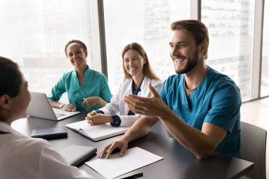 Bir grup gülen tıp çalışanı konferans odasında masada oturuyor, arkadaşça olumlu bir sohbet yürütüyor, ortak görevi tartışıyor, ortak tavsiye ve görüşleri paylaşıyor, takım çalışması ve işbirliğinden memnun görünüyorlar.
