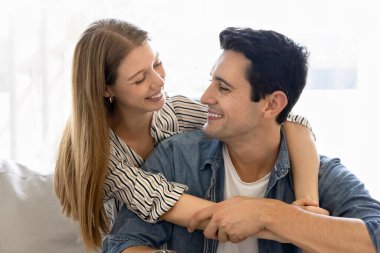 Mutlu genç Latin eş arkadan neşeli kocayı kucaklıyor. Sıcak bir evde rahat rahat oturup sohbet eden, gülümseyen, gevezelik eden pozitif bir çift.